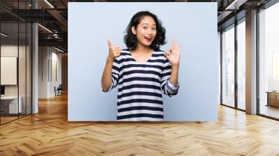 Asian young woman over isolated blue background showing ok sign and thumb up gesture Wall mural