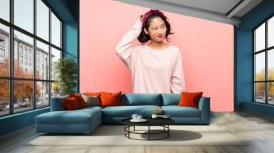 Asian young woman over isolated pink background having doubts while scratching head Wall mural