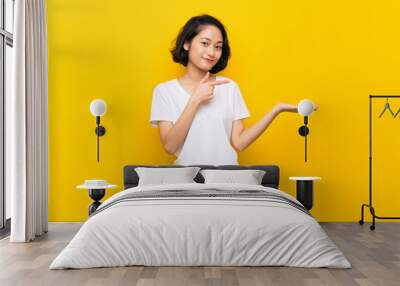 Asian young woman over isolated yellow wall holding copyspace imaginary on the palm to insert an ad Wall mural