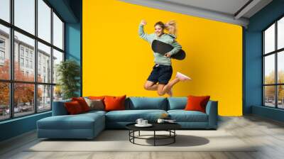 Blonde teenager skater girl jumping over isolated yellow background Wall mural