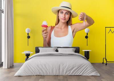 Blonde Uruguayan girl in summertime holding ice cream isolated on yellow background showing thumb down with negative expression Wall mural