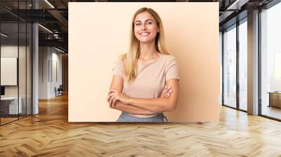 Blonde Uruguayan girl isolated on beige background keeping the arms crossed in frontal position Wall mural