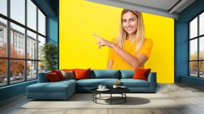 Blonde Uruguayan girl isolated on yellow background pointing to the side to present a product Wall mural