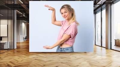 Blonde woman over isolated blue background holding copyspace to insert an ad Wall mural