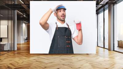 Butcher caucasian man wearing an apron and serving fresh cut meat over isolated white background doing surprise gesture while looking to the side Wall mural