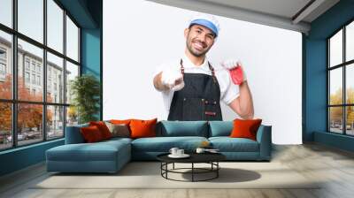 Butcher caucasian man wearing an apron and serving fresh cut meat over isolated white background pointing front with happy expression Wall mural