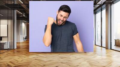 Caucasian handsome man celebrating a victory over isolated purple background Wall mural