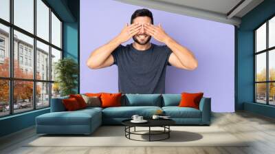 Caucasian handsome man covering eyes by hands and smiling over isolated purple background Wall mural