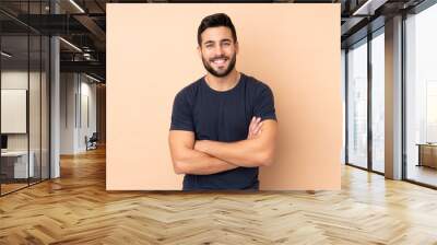 Caucasian handsome man isolated on beige background keeping the arms crossed in frontal position Wall mural