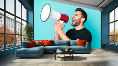 Caucasian handsome man isolated on blue background shouting through a megaphone Wall mural