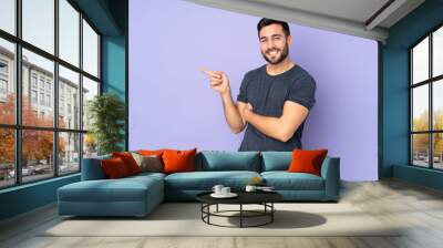 Caucasian handsome man pointing finger to the side over isolated purple background Wall mural