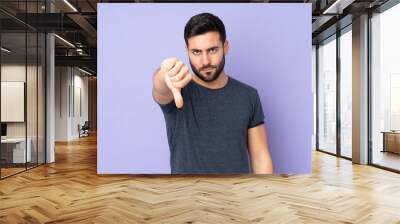 Caucasian handsome man showing thumb down with negative expression over isolated purple background Wall mural