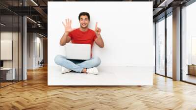 Caucasian handsome man with a laptop sitting on the floor counting six with fingers Wall mural