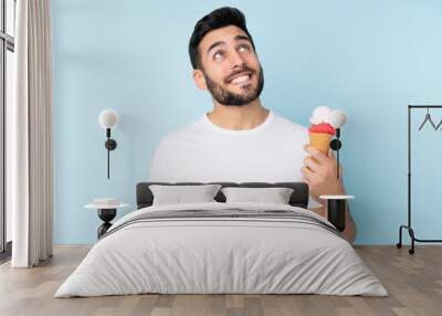 Caucasian man with a cornet ice cream isolated on blue background looking up while smiling Wall mural