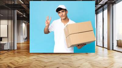 Delivery Argentinian man isolated on blue background happy and counting three with fingers Wall mural