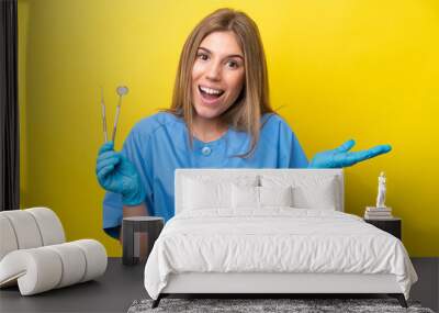 Dentist caucasian woman holding tools isolated on yellow background with shocked facial expression Wall mural