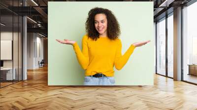 Dominican woman over isolated green background holding copyspace with two hands Wall mural