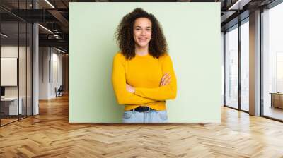 Dominican woman over isolated green background keeping the arms crossed in frontal position Wall mural