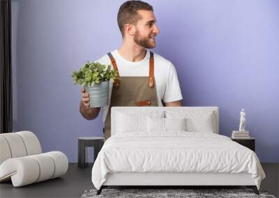 Gardener caucasian man holding a plant isolated on yellow background looking side Wall mural