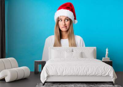 Girl with christmas hat over isolated background having doubts and with confuse face expression Wall mural