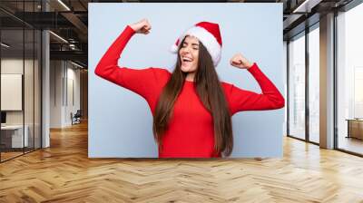 Girl with christmas hat over isolated blue background celebrating a victory Wall mural