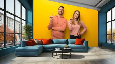 Group of two people on yellow background showing and lifting a finger in sign of the best Wall mural