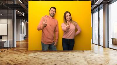 group of two people on yellow background smiling and showing victory sign Wall mural