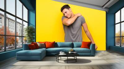 Handsome man over isolated yellow wall suffering from pain in shoulder for having made an effort Wall mural