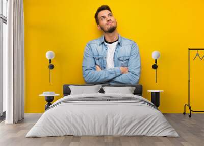 Handsome man over yellow wall looking up while smiling Wall mural