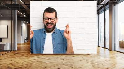 Handsome man with beard over white brick wall with fingers crossing Wall mural