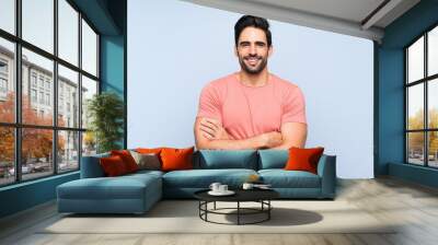 Handsome young man in pink shirt over isolated blue background keeping the arms crossed in frontal position Wall mural