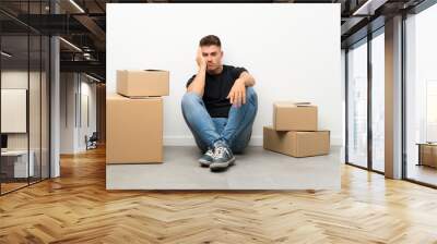 Handsome young man moving in new home among boxes unhappy and frustrated Wall mural