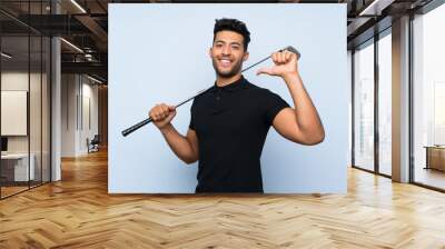 Handsome young man playing golf over isolated blue background proud and self-satisfied Wall mural