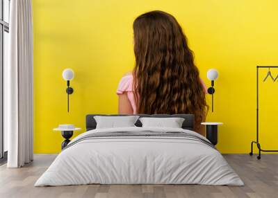 Little caucasian girl isolated on yellow background in back position and looking side Wall mural