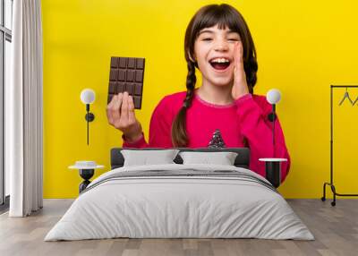 Little caucasian girl with chocolat isolated on yellow background with surprise and shocked facial expression Wall mural