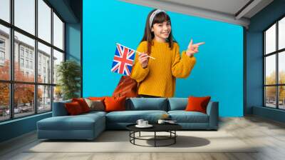 Little girl studying English isolated on blue background pointing finger to the side Wall mural