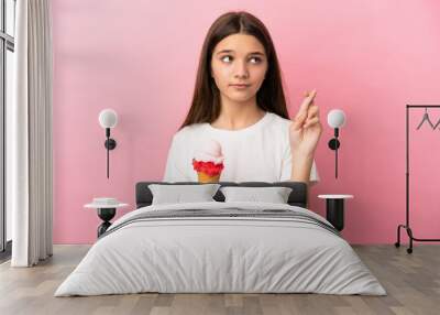 Little girl with a cornet ice cream over isolated pink background with fingers crossing and wishing the best Wall mural