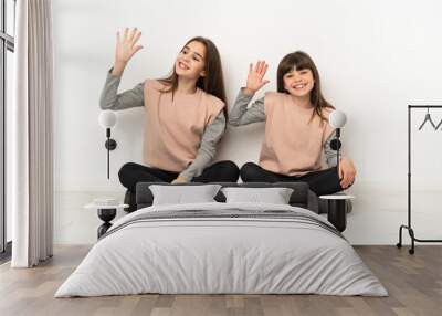 Little sisters sitting on the floor isolated on white background saluting with hand with happy expression Wall mural