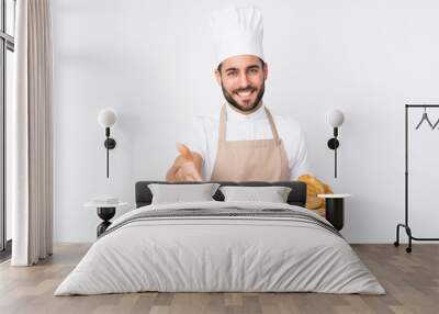 Male baker holding a table with several breads isolated on white background handshaking after good deal Wall mural