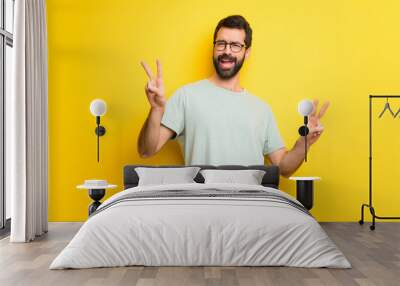 Man with beard and green shirt smiling and showing victory sign with both hands Wall mural