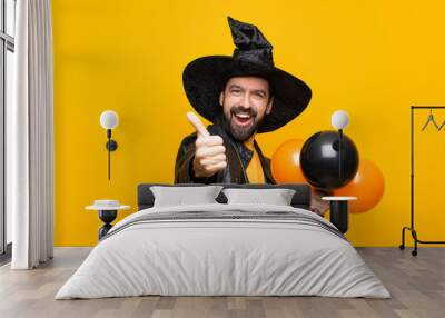 Man with witch hat holding black and orange air balloons for halloween party with thumbs up because something good has happened Wall mural