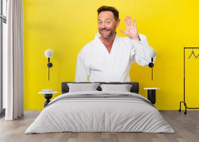 Middle age caucasian man doing karate isolated on yellow background saluting with hand with happy expression Wall mural