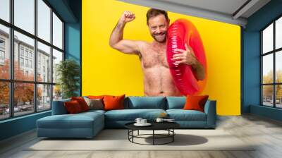 Middle age caucasian man holding inflatable donut isolated on yellow background doing strong gesture Wall mural