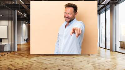 Middle age caucasian man isolated on beige background pointing front with happy expression Wall mural