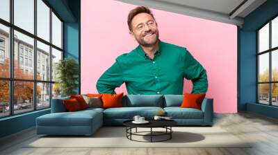 Middle age caucasian man isolated on pink background posing with arms at hip and smiling Wall mural