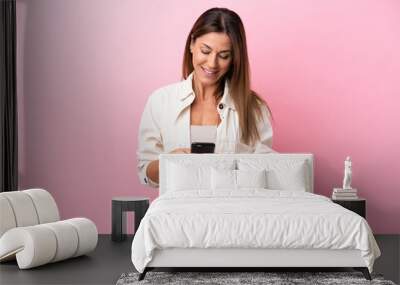 Middle age caucasian woman isolated on pink background sending a message with the mobile Wall mural