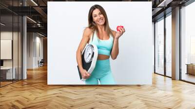 Middle age caucasian woman isolated on white background with weighing machine and with an apple Wall mural