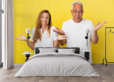 Middle age couple isolated on yellow background having doubts and with confuse face expression Wall mural