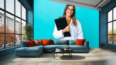 Middle age woman isolated on blue background wearing a doctor gown and holding a folder Wall mural