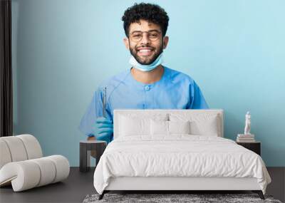 Moroccan dentist man holding tools isolated on blue background smiling a lot Wall mural